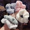 Une main tient plusieurs élastiques pour cheveux en tricot doux de couleurs pastel, bleu clair, rose et blanc.