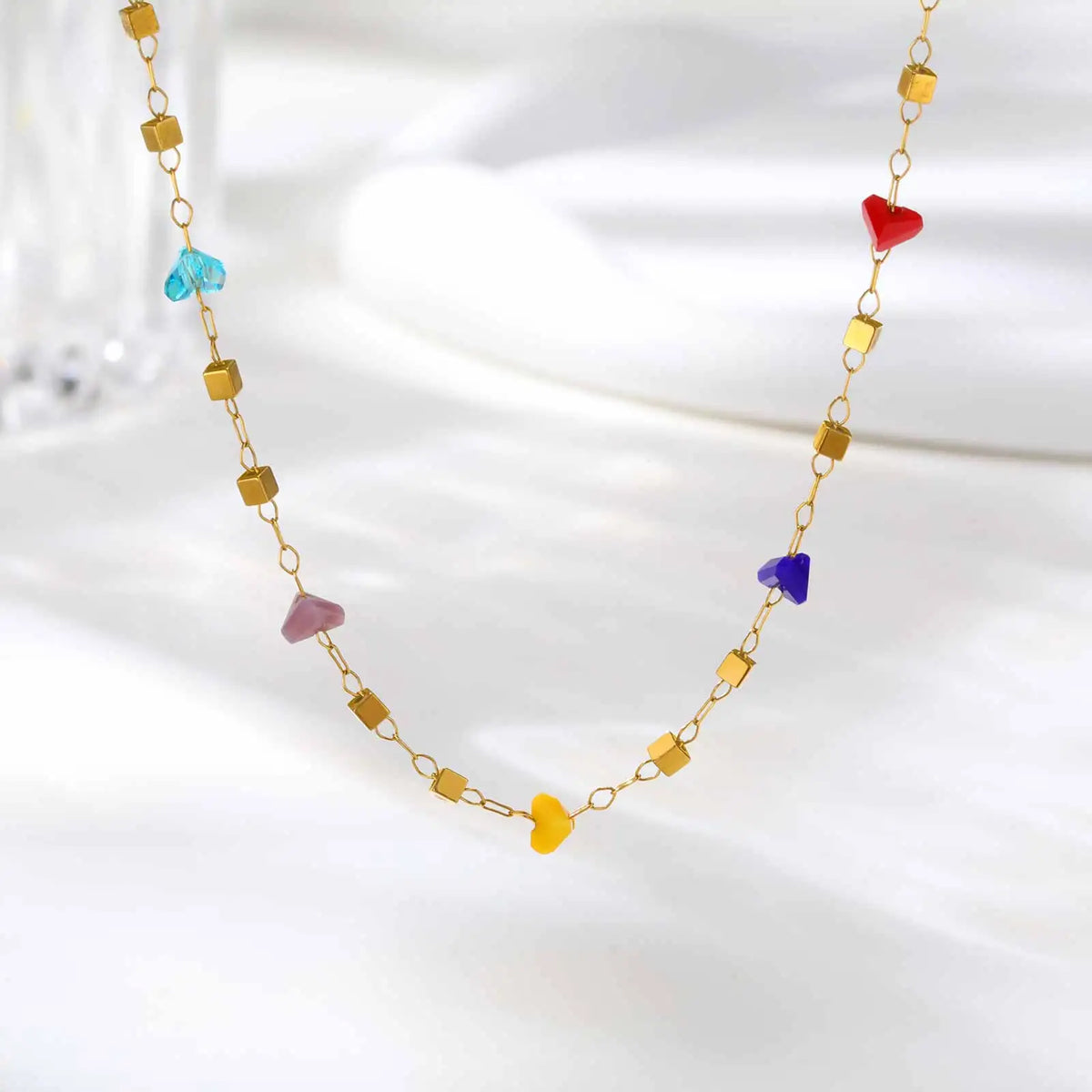 A delicate gold chain necklace featuring irregular colored gemstone charms like blue, purple, and red heart shapes.