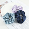A set of three satin scrunchie headbands in lavender, dusty blue, and navy are displayed on a white plate.
