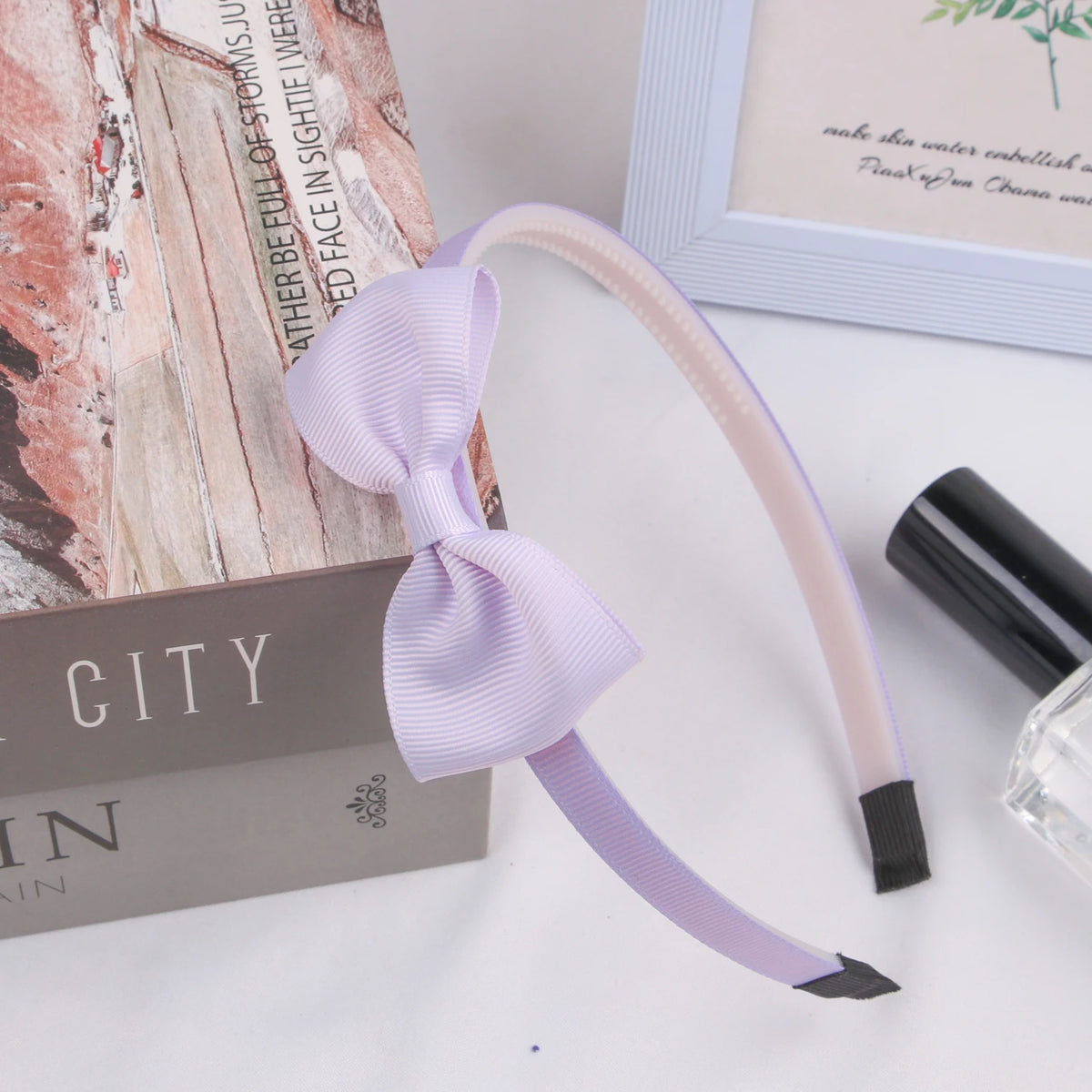 A light purple grosgrain ribbon hair bow with a black accent is displayed next to a book and a picture frame.