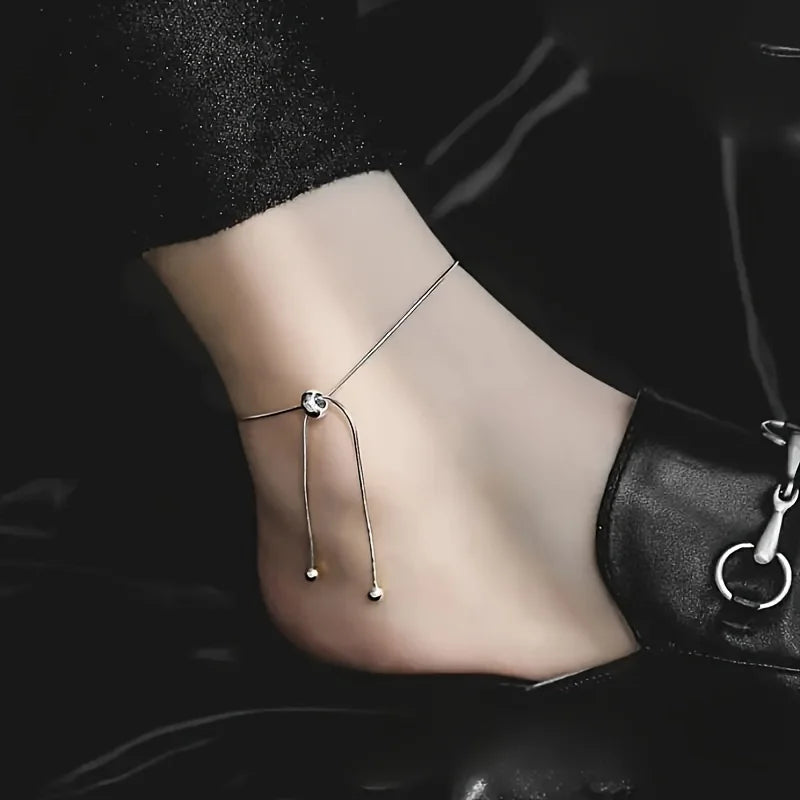 Gros plan d'une main portant un anklet argenté réglable et extensible à la cheville.