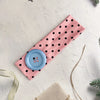 Pink fabric headband with black polka dots and a light blue accent piece on a white background.