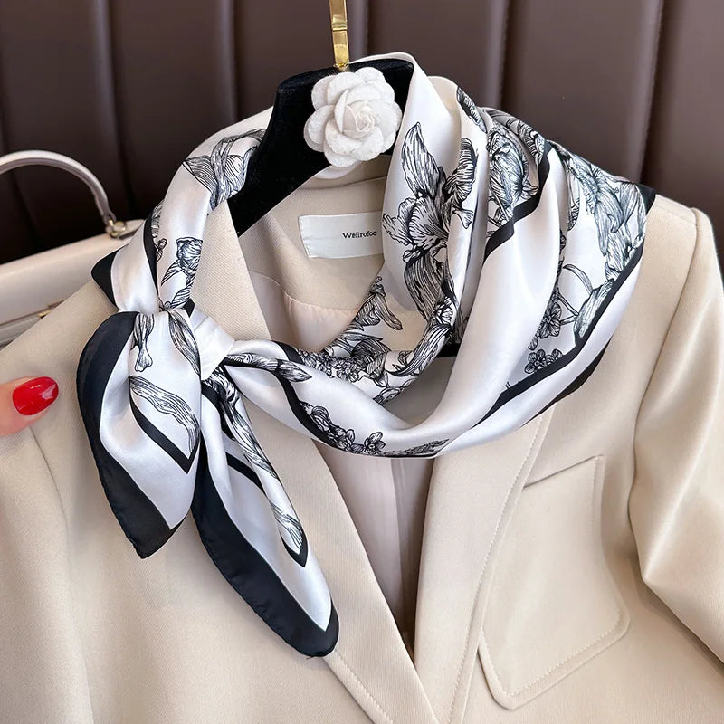 A white and black patterned silk scarf tied in a bow draped around a beige blazer.