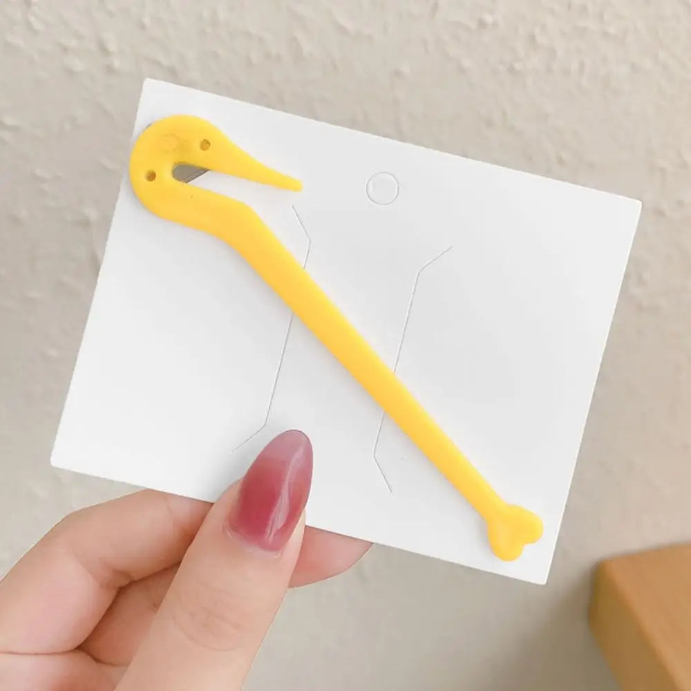 A yellow hair elastic and rubber band remover tool is shown against a white card, held by a hand.
