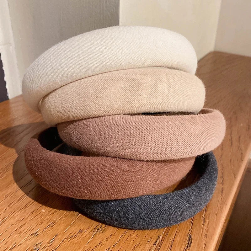 Une pile de bandeaux pour cheveux épaissis de couleur café, dans diverses nuances de beige et de brun, sur une surface en boi
