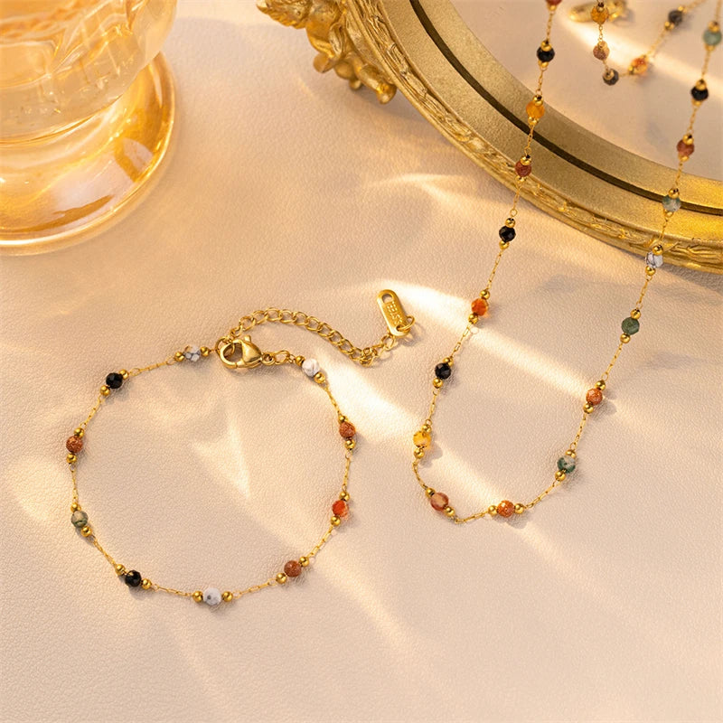 A gold-toned beaded jewelry set featuring amber, green, and black stones displayed next to a decorative mirror.