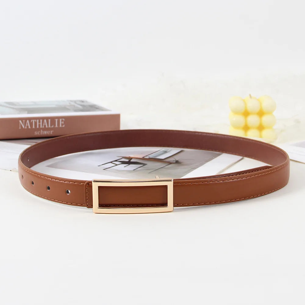 A brown faux leather belt with a gold buckle is displayed on a white background next to a book and some yellow beads.
