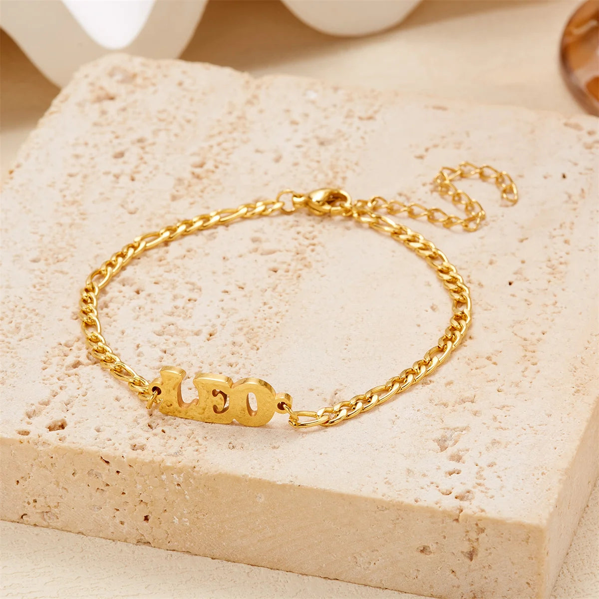 Gold stainless steel zodiac constellation charm bracelet resting on a light beige stone surface.