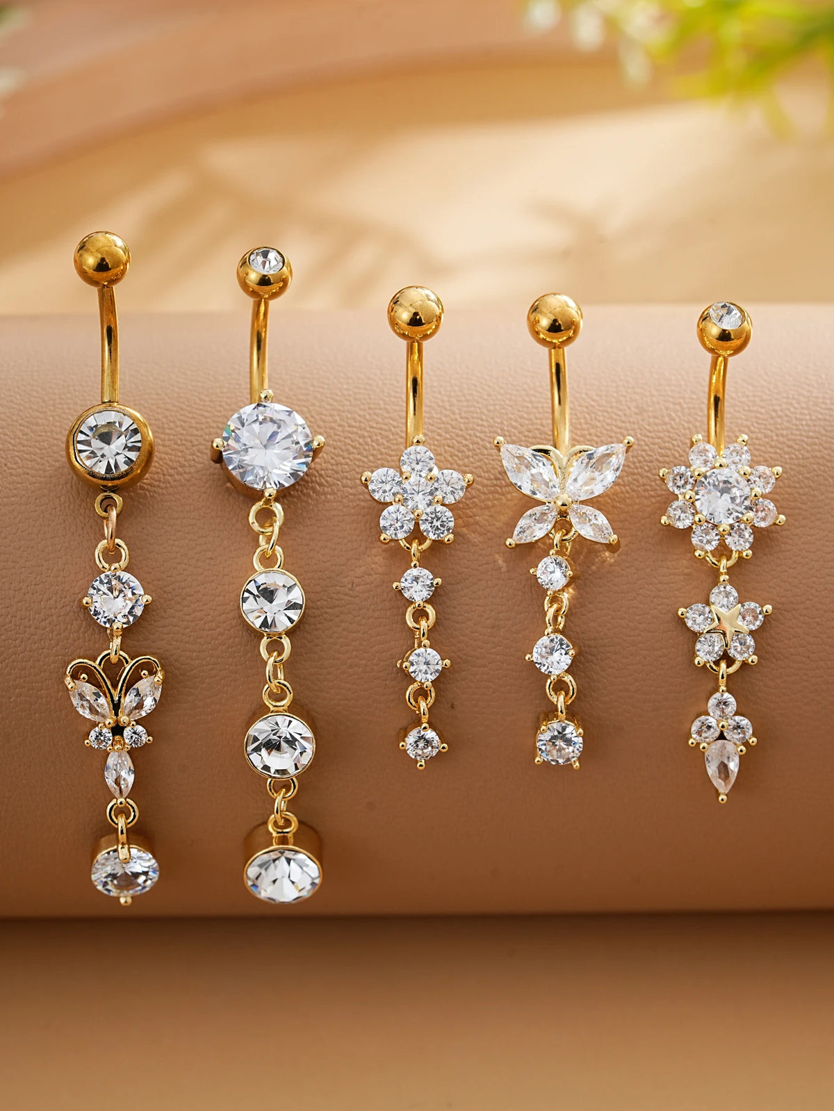 A set of five gold stainless steel dangled belly button rings featuring clear and diamond-cut stones.