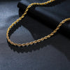 A close-up of a dainty gold rope chain necklace lying on a dark fabric background.