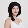 A woman wearing a black silk sleep bonnet with a white top, looking directly at the camera.