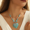 Rapproché d'un pendentif en forme de cœur turquoise porté autour du cou sur peau claire et tissu blanc.