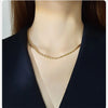 A close-up of a dainty gold rope chain necklace worn around the neck against a dark blazer.