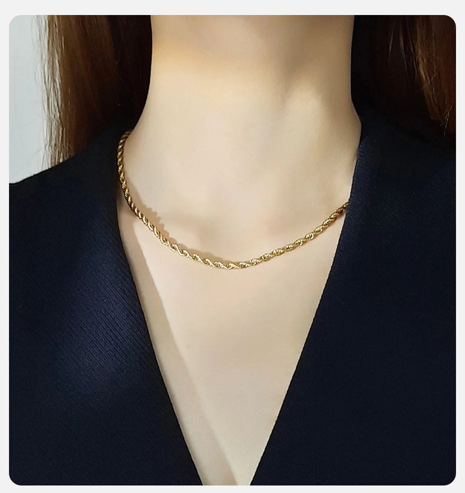 A close-up of a dainty gold rope chain necklace worn around the neck against a dark blazer.