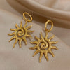 Boucles d'oreilles pendantes en spirale de tournesol plaquées or, présentées sur un tissu neutre.