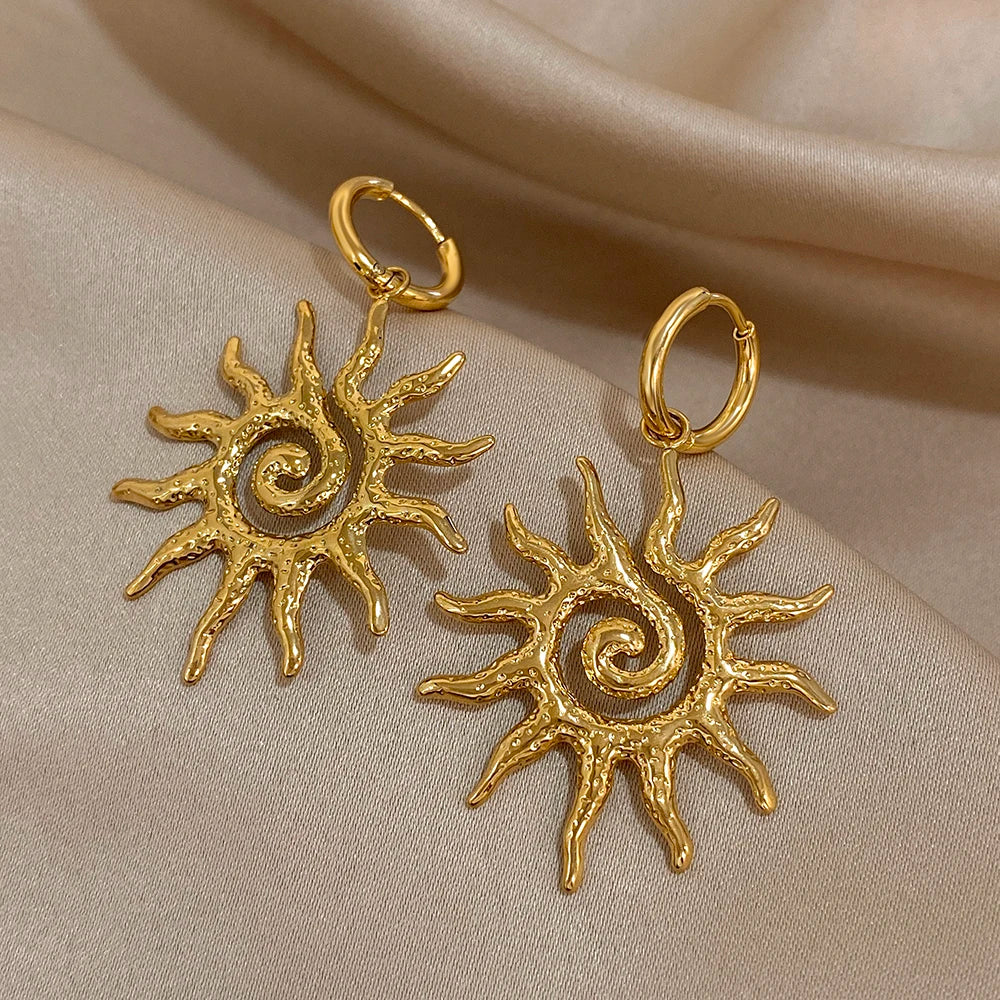 Boucles d'oreilles pendantes en spirale de tournesol plaquées or, présentées sur un tissu neutre.