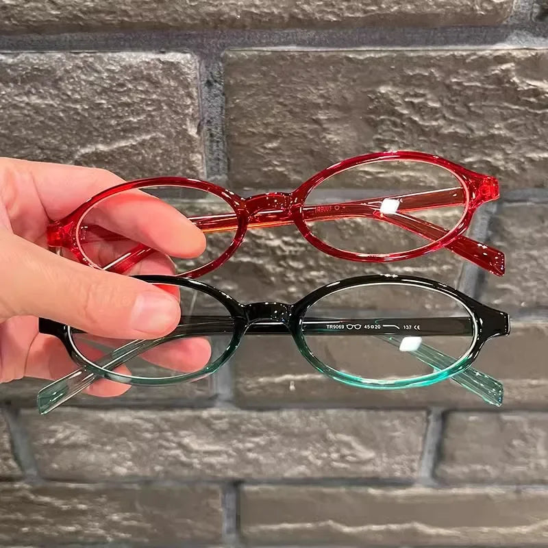 Une main tient une paire de lunettes de mode ovales rétro Y2K, avec des montures rouges et vertes.