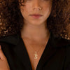 A close-up of a woman wearing a gold initial name crown pendant necklace under a black blazer.