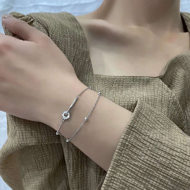 Sterling silver double heart charm bracelet worn on a wrist against a light olive green top