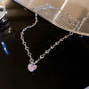 A delicate silver heart necklace featuring pink stones and zircon accents displayed on a dark surface.