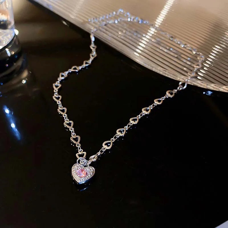 A delicate silver heart necklace featuring pink stones and zircon accents displayed on a dark surface.