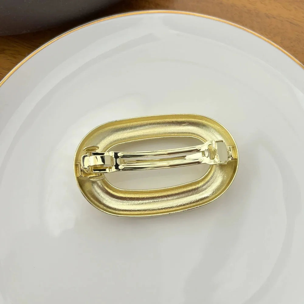 A gold-colored metal oval hair clip resting on a white plate.