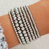 A stack of silver round beaded bracelets worn on a person's wrist.