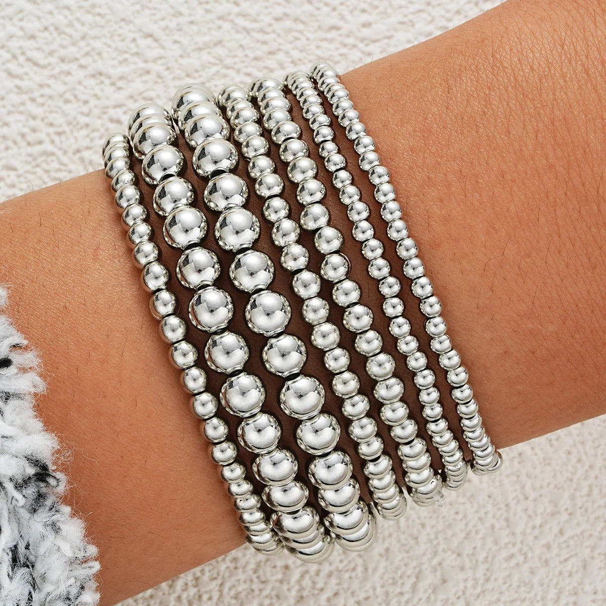 A stack of silver round beaded bracelets worn on a person's wrist.