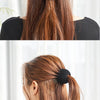 A woman is shown tying an elegant black horsetail hair clip into a ponytail on her long brown hair.