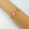 Gold plated stainless steel double-sided petal bracelet with pink floral charms on a beige textured background