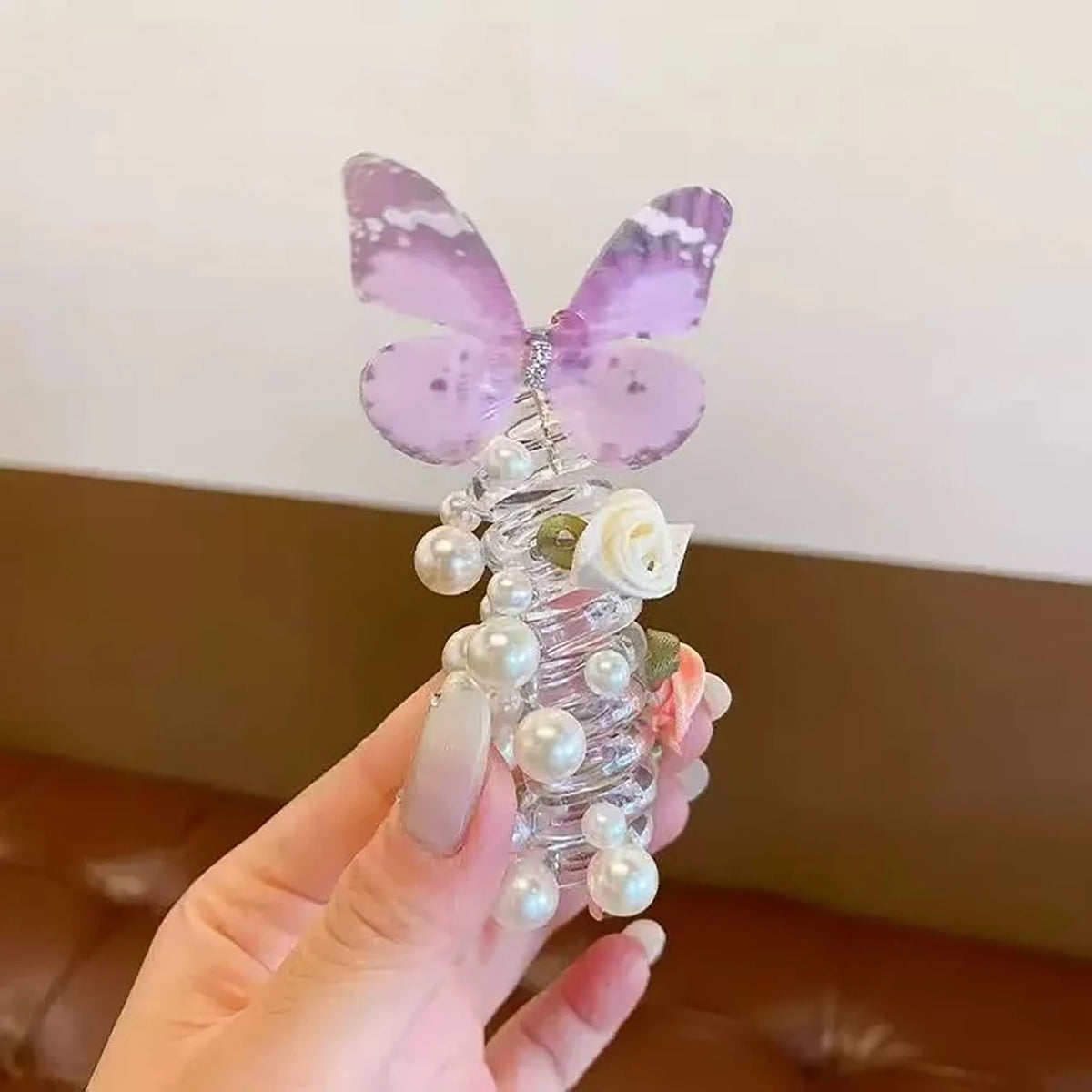 A hand holds a decorative item featuring a purple butterfly made of pearls and clear strands.