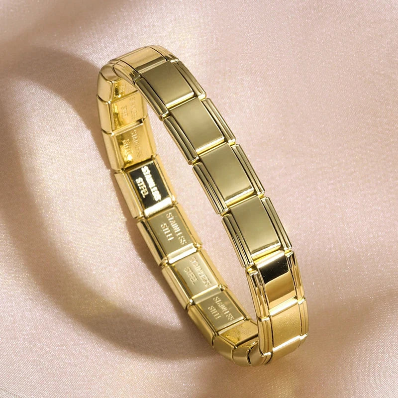 A close-up shot of a gold stainless steel charm bracelet on a light pink background.