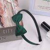 A dark green grosgrain ribbon hair bow is displayed next to a book and a small glass container.