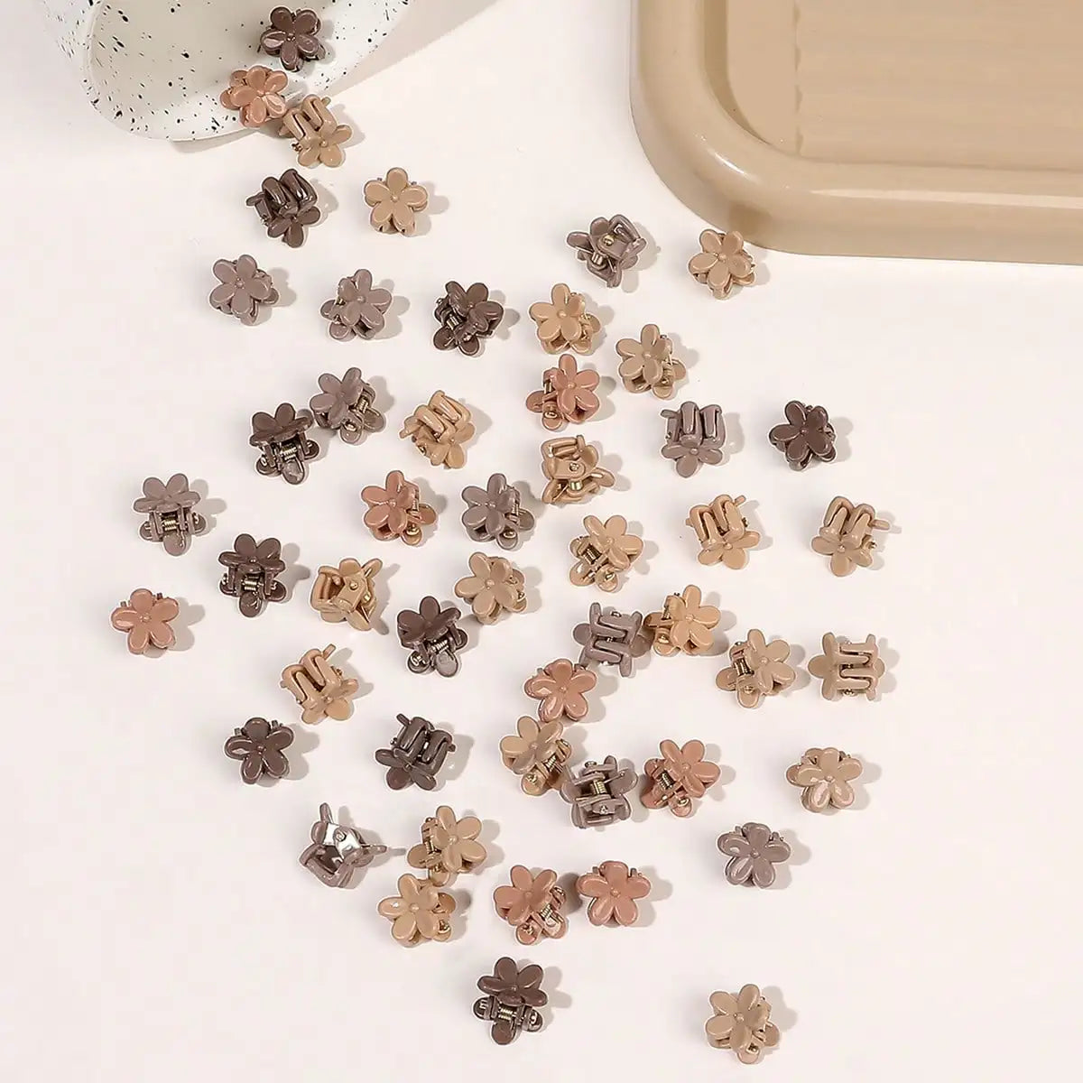 A collection of small, rose gold and gray mini flower hair clips scattered on a white surface.
