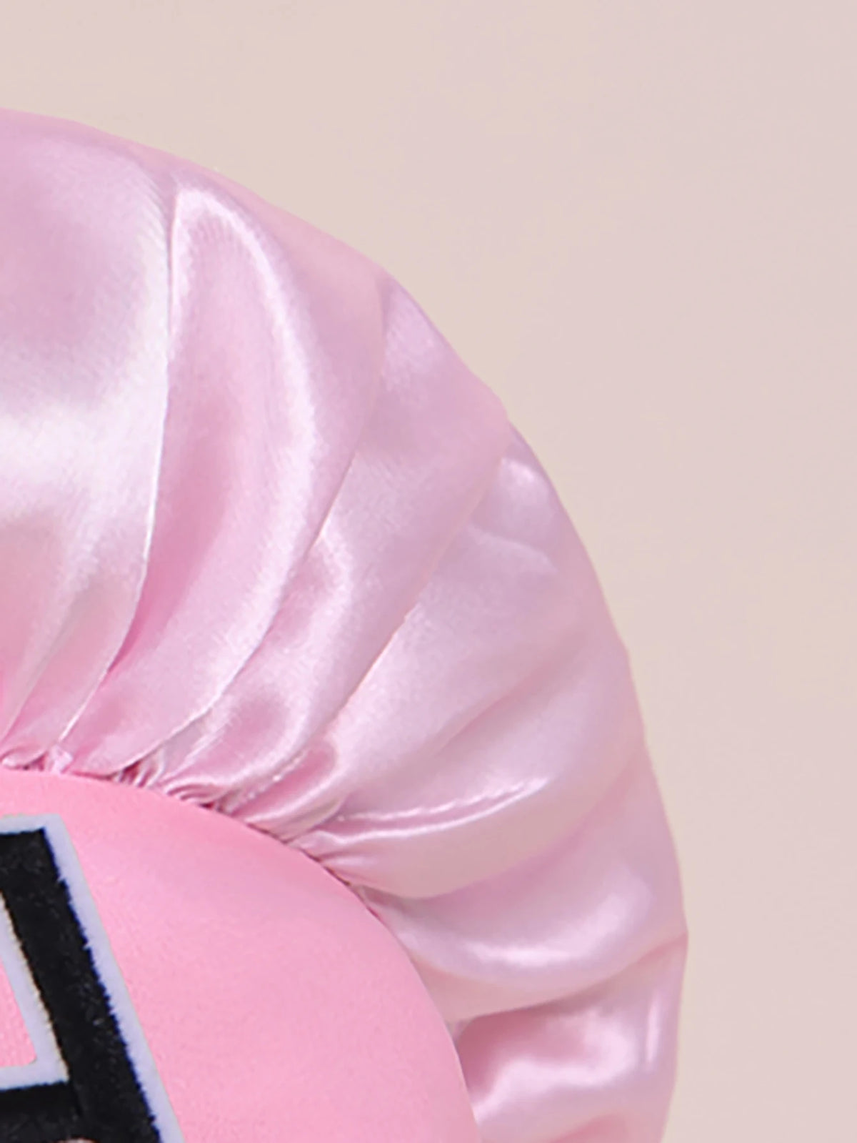 Pink satin sleep cap with a ruffled design and a black letter detail