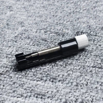A black precision watch link pin remover tool is shown against a gray textured background.