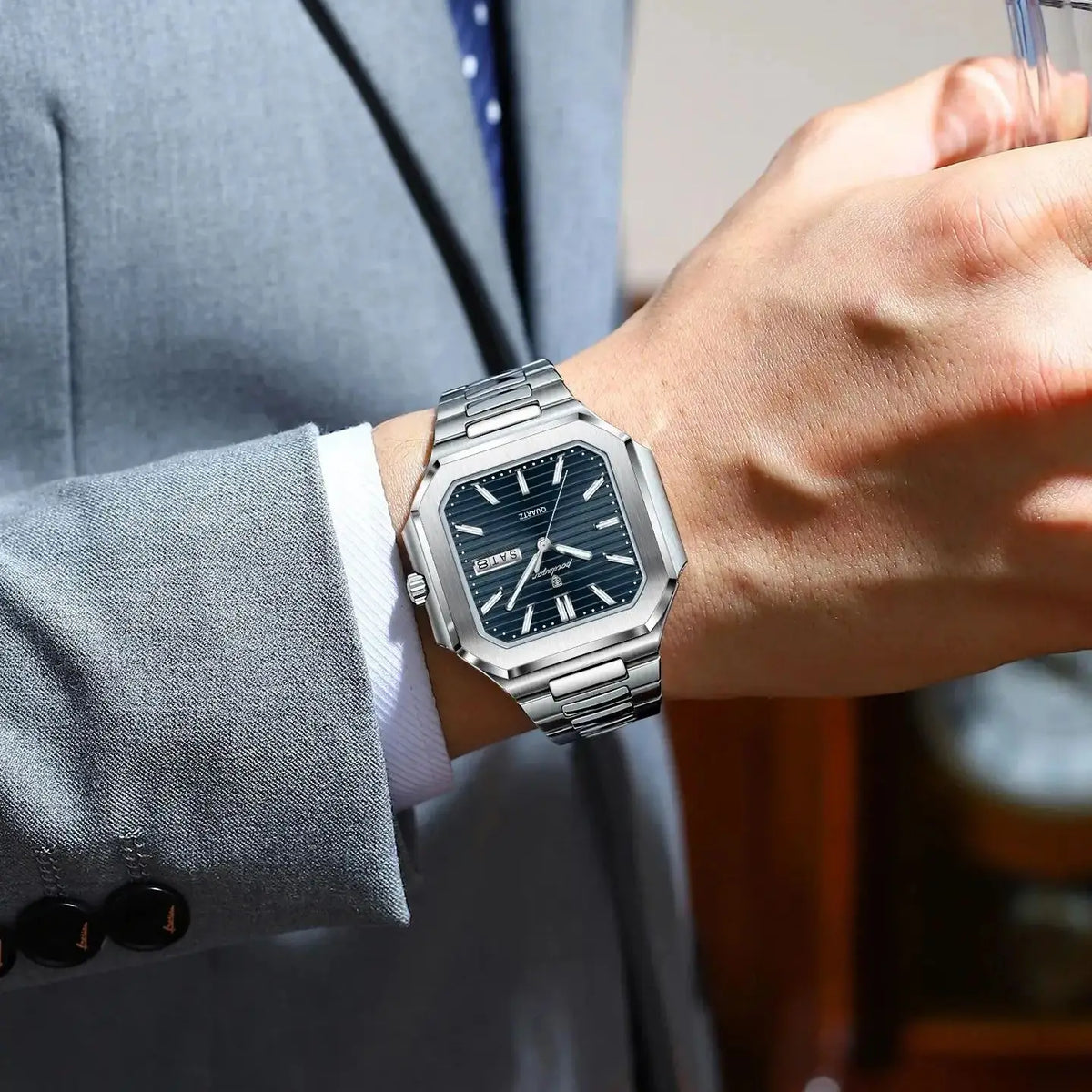 A close-up of a man wearing a stainless steel quartz watch on his wrist while in a suit jacket.