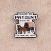 An enamel pin featuring a silhouette of horses and the text PLEASE BE PATIENT WITH ME I'M FROM THE 1900s
