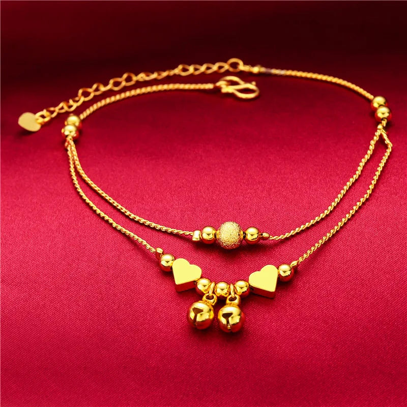 Gold-plated heart bell anklets for women displayed on a red fabric background