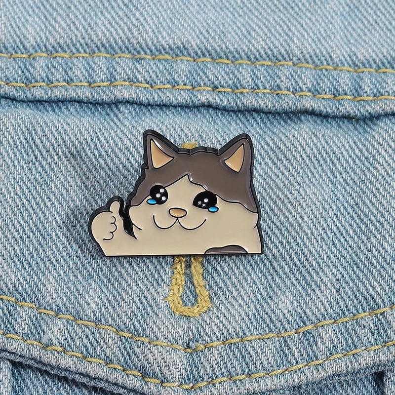 A cute cat face enamel brooch pin with blue eyes and a smiling expression pinned on denim fabric.