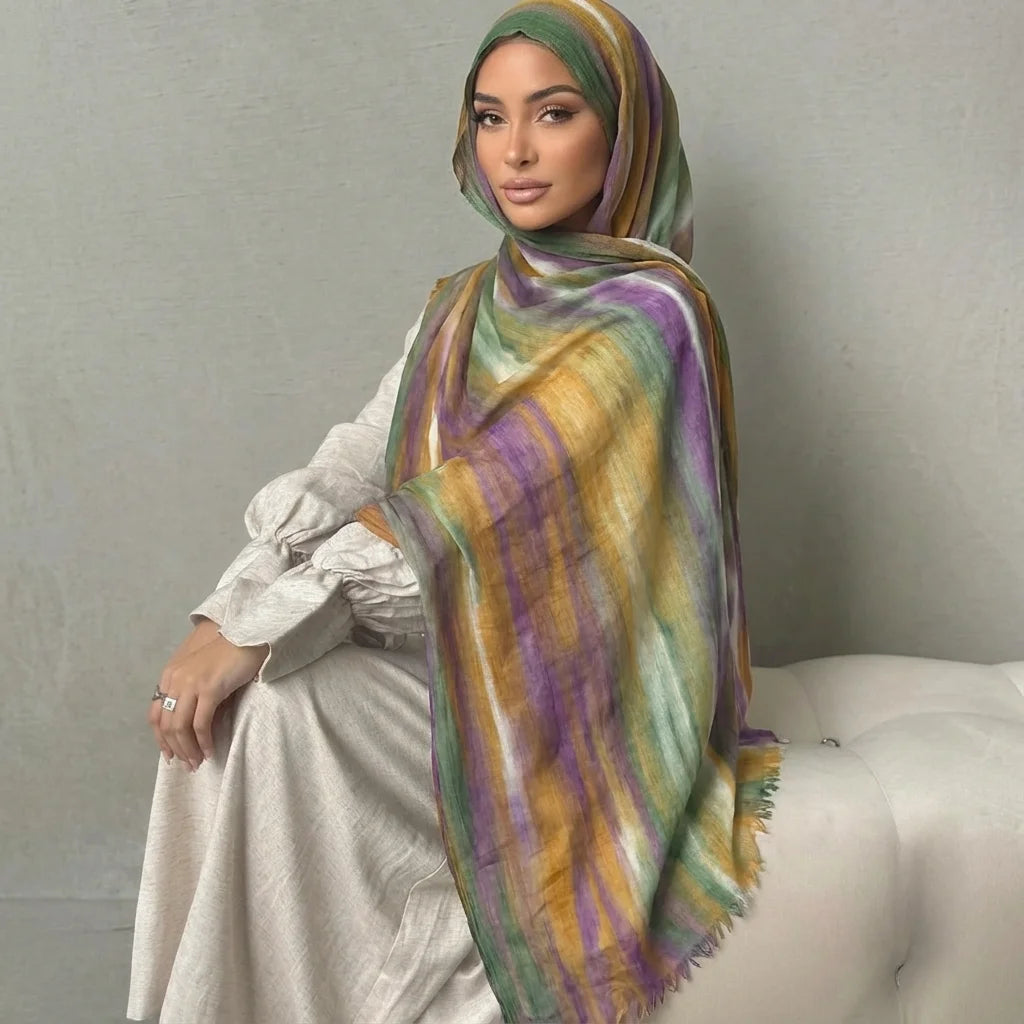 Una mujer vistiendo un elegante pañuelo de hijab a rayas en tonos morados, amarillos y verdes, sobre una prenda de color clar