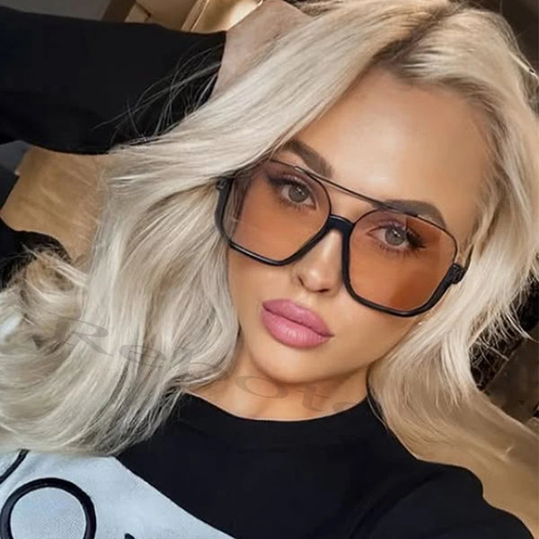 صورة مقربة لامرأة بشعر أشقر طويل ترتدي نظارات شمسية مربعة كبيرة.