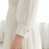 Close-up of a cream-colored dress sleeve featuring a delicate white flower button cover.