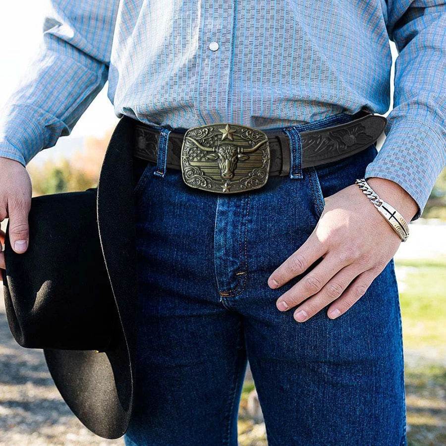 Una persona vistiendo una camisa y jeans de mezclilla con un cinturón western grabado y un sombrero negro.
