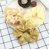 A set of three yellow and white knitted hair scrunchie headbands displayed on a white plate.