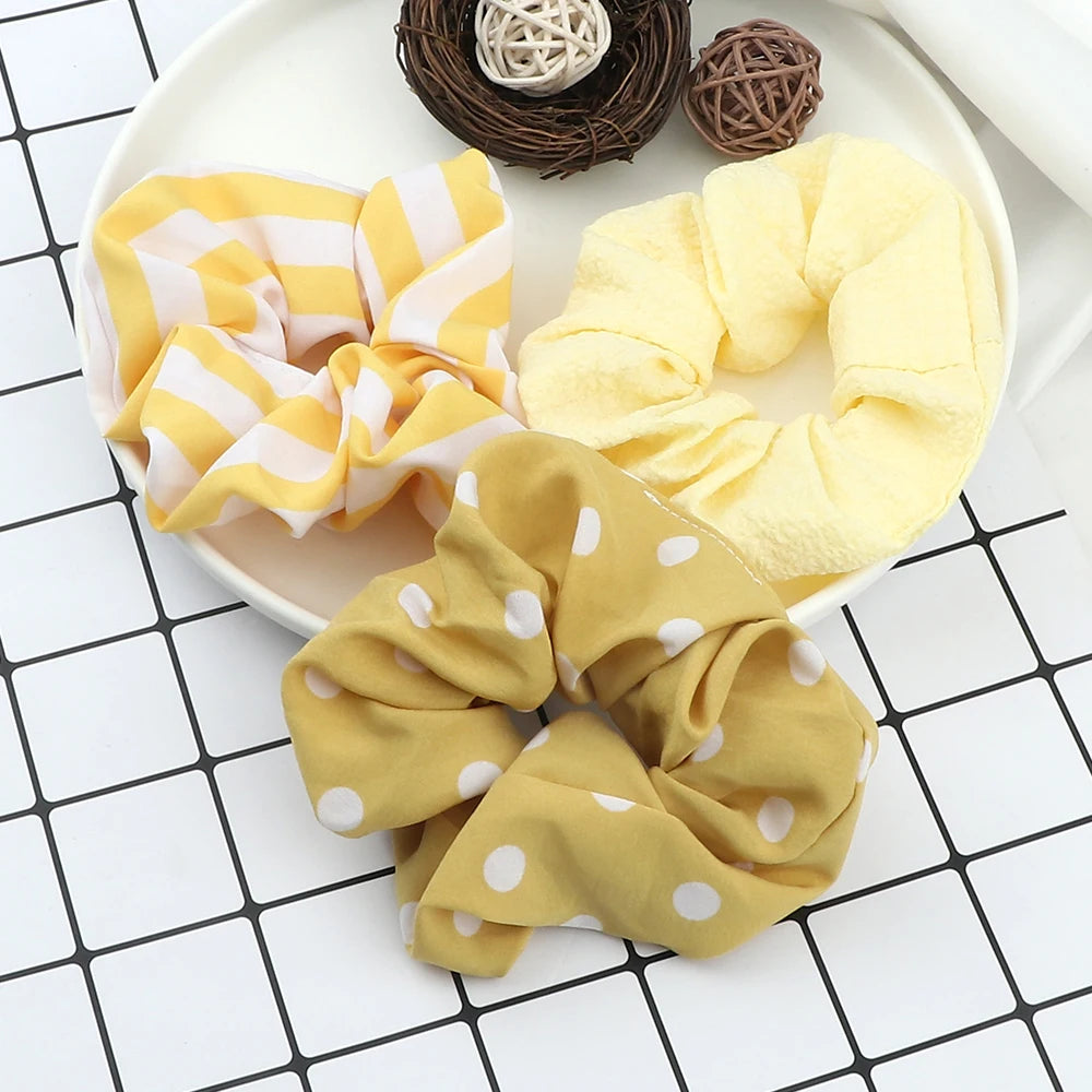 A set of three yellow and white knitted hair scrunchie headbands displayed on a white plate.