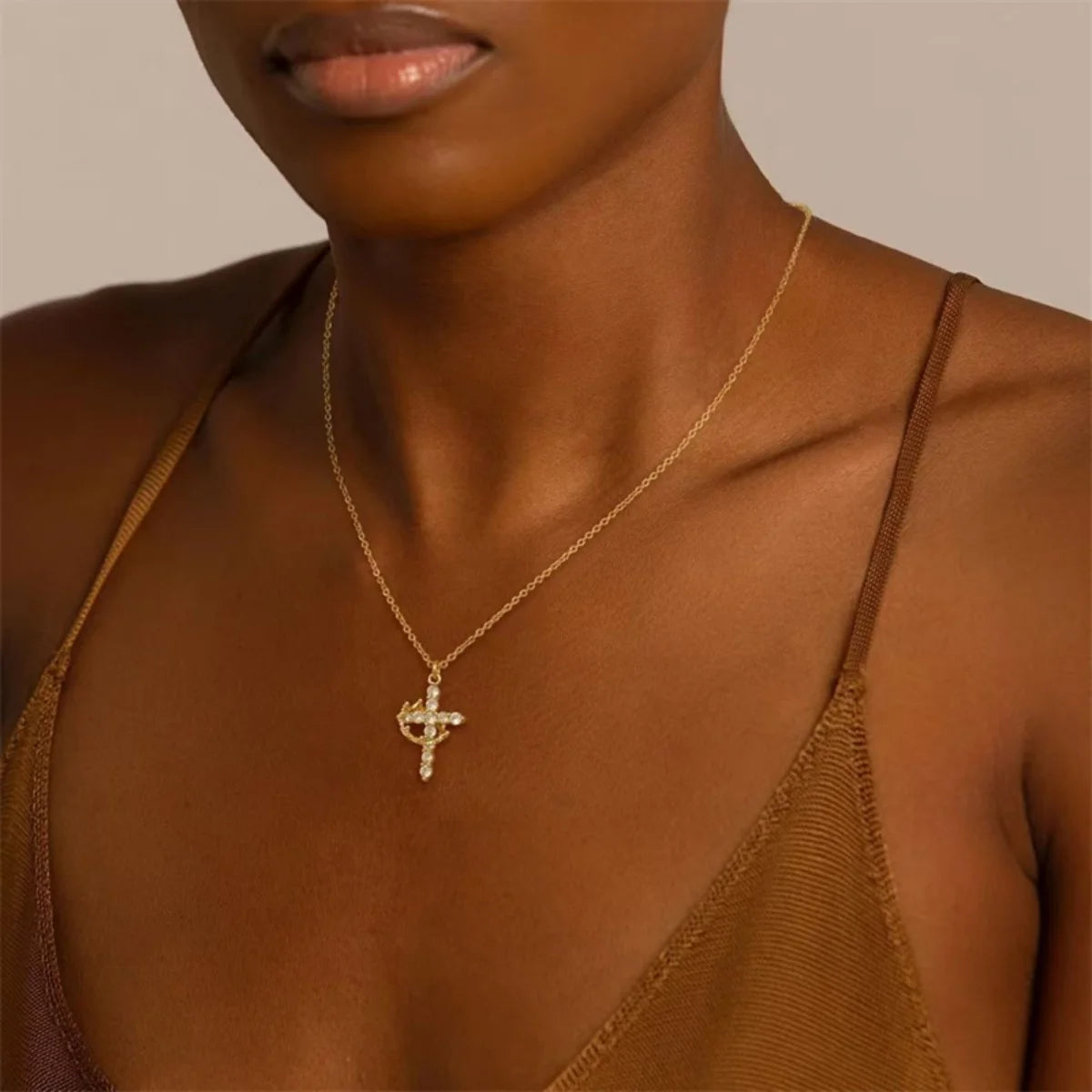 A close-up of a woman wearing a gold-toned cross pendant necklace on her neck.