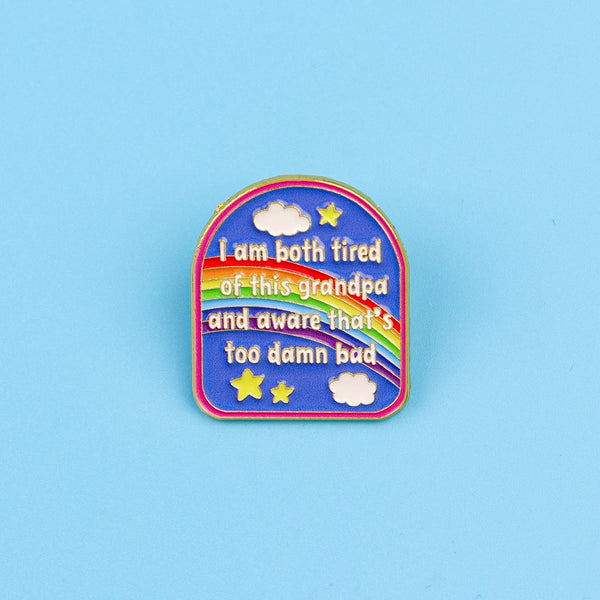A colorful enamel pin featuring text that reads I am both tired of this grandpa and aware that's too damn bad surrounded by s