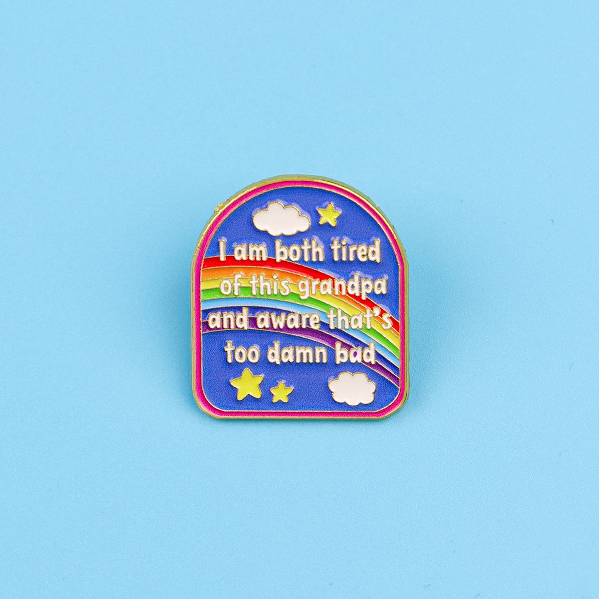 A colorful enamel pin featuring text that reads I am both tired of this grandpa and aware that's too damn bad surrounded by s