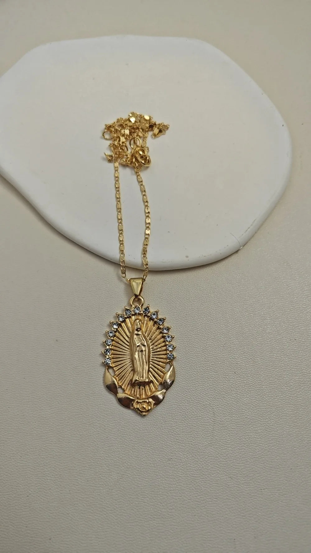 A dainty golden Christian necklace featuring a figure of the Virgin Mary surrounded by small stones.
